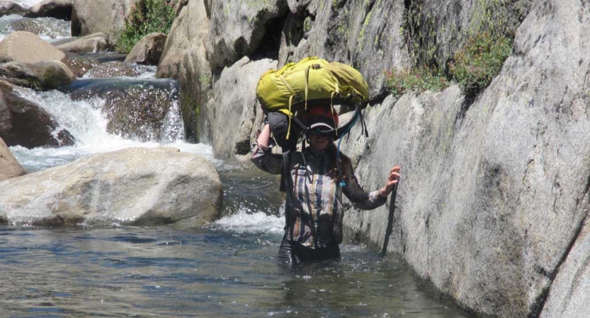A person wades through waist-deep water and carries their backpack on their head